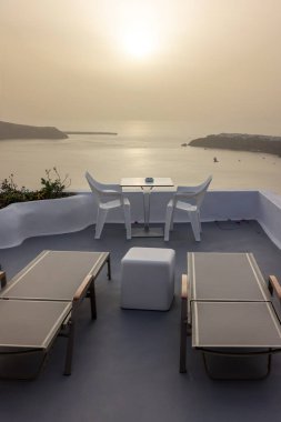 Yunanistan 'ın Santorini kentindeki Imerovigli köyünde güneş pansiyonları ve sandalyeler, günbatımının muhteşem manzarasıyla birlikte. 