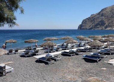 Kamari, Santorini, Yunanistan - 30 Haziran 2021: Santorini 'deki siyah volkanik Kamari plajında güneşlik. Cyclades, Yunanistan