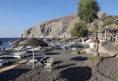 Kamari, Santorini, Yunanistan - 3 Temmuz 2021: Santorini 'deki siyah volkanik Kamari plajında güneşlik. Cyclades, Yunanistan