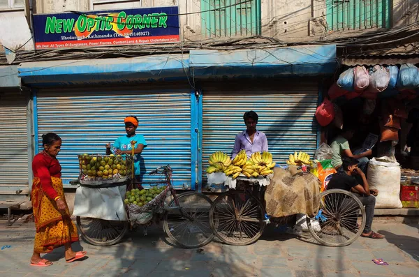 ネパールのカトマンズ 2019年6月19日 自転車の果物販売者は カトマンズの通りでバナナとマンゴーを販売しています 古いナポリの女性が赤い伝統的な服 通りのベンダーを歩く — ストック写真