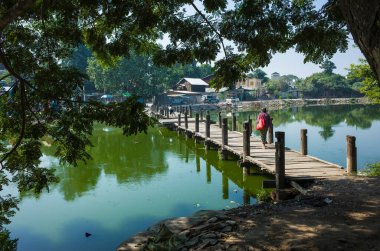 Mandalay, Myanmar - 9 Ocak 2019: Yeşil su kanalı üzerinde küçük tahta bir köprüde yürüyen kadın