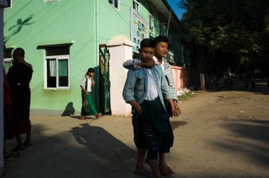 Amarapura, Mandalay, Myanmar - 14 Ocak 2020: Çocuklar okul kapısından çıkın. İki genç çocuk etrafta takılıyor ve şakacı bir şekilde sarılıyorlar.