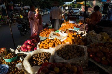 Mandalay, Myanmar - 15 Ocak 2020 Zay Cho Pazarı. Meyve tezgahının yanındaki Budist rahibeler. Güneş ışığı turuncu mandalinalarda parlıyor. Sokak fotoğrafçılığı.