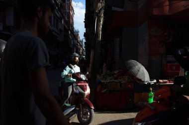 Katmandu, Nepal - 20 Haziran 2019: Güneş Nepalli genç bir kadının üzerinde parlıyor, eski bir kasabada, yerel hayatın dar sokaklarında scooter sürüyor.