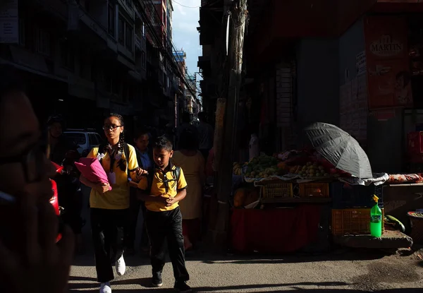 Kathmandu, Nepal - 20 Haziran 2019: Güneş iki okul çocuğu üzerine parlıyor, kardeş ve kardeş eski kasabadaki dar yolda yürüyor, yerel günlük yaşam