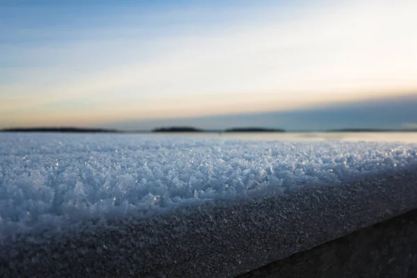 Snow frost abstract winter background close-up bokeh, Cold season rime ice crystals on wooden embankment of lake Malaren, evening sky, Vasteras, Sweden