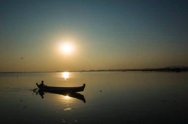 Güneş batarken Taung Tha Man Gölü 'nde gölün karşısında balıkçı teknesi silueti. Amarapura, Mandalay, Myanmar