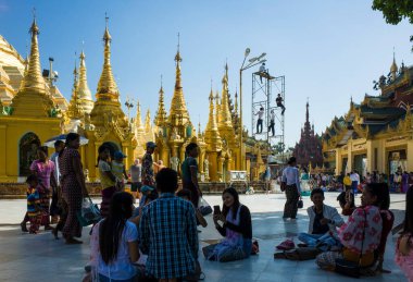 Yangon, Myanmar - 23 Aralık 2019: Birmanya halkı gölgede oturuyor ve elektrikçiler Myanmar 'ın en kutsal Budist pagodası olan Shwedagon' da lamba bakımı üzerinde çalışıyorlar.