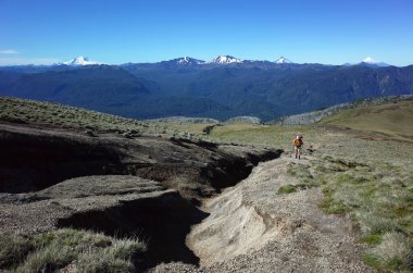 Patagonya 'da yürüyüş, Şili' nin Los Lagos bölgesindeki Puyehue Ulusal Parkı 'ndaki Puyehue yanardağında tek başına yürüyen bir adam. Volkanlar Tronador, Antillanca, Kazablanka, Puntiagudo, Osorno ufukta