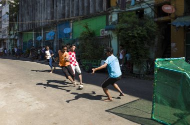 Yangon, Myanmar - December 22, 2019: Football on shabby street barefoot on asphalt. Daily life clipart