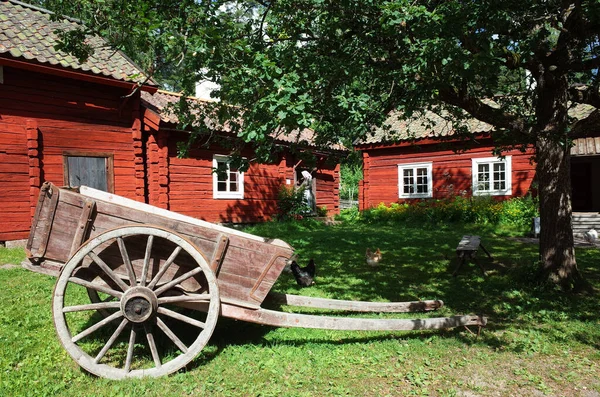 Vasteras スウェーデン 7月3 2019 バルビー野外博物館 スウェーデンの伝統的な赤の家に囲まれた庭の緑の芝生の上の大きな車輪の上に古い木製のカート 夏の晴れた日 — ストック写真