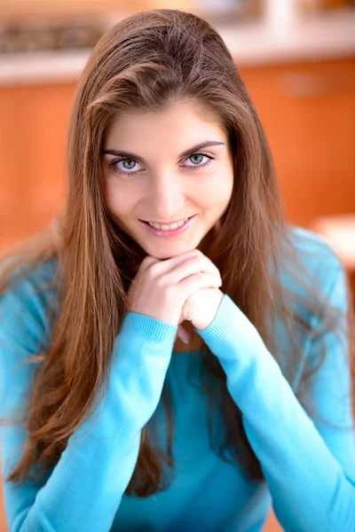 Retrato de uma bela jovem sentada na cozinha em casa e sorrindo — Fotografia de Stock