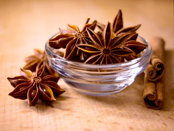 Estrella anís en el tazón de cristal y palos de canela en la mesa de madera — Foto de Stock