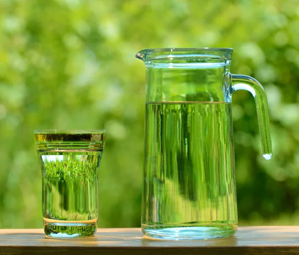 Un verre et une carafe pleins d'eau sur le fond de feuillage — Photo