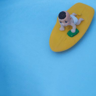 Rüzgar sörfü tahtasında yeşil arabalı bir bebek. Açık mavi arkaplan. Estetik sahne.