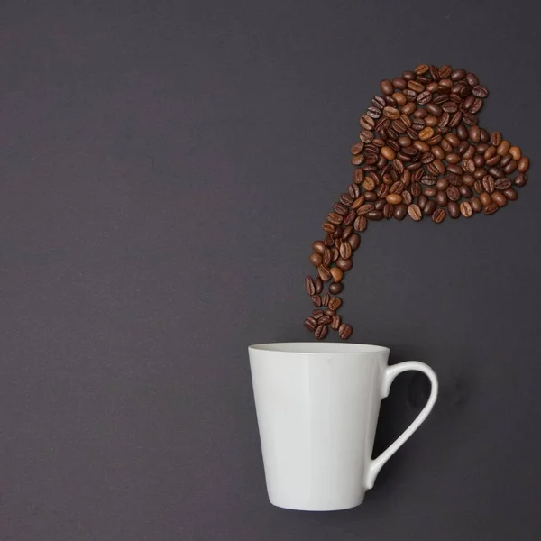Kalp şeklinde kahve çekirdekleri fincandan siyah arka planda fotokopi alanı ile birlikte çıkar. Minimalist düz yatış sahnesi.