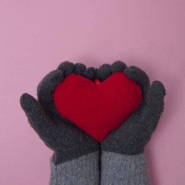 Gri eldivenli kadın eller pembe arka planda bir aşk kalbi tutuyor. Düz uzanan en küçük sahne.