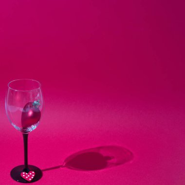 Aşk ifadesi olarak, kırmızı arka planda, gölgeli bir şarap kadehinde. Minimalist sahne.