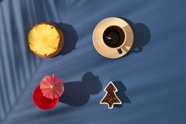 Ananaslı kahve molası, şemsiyeli içki ve mavi arka planda palmiye yaprakları. Minimalist sahne.