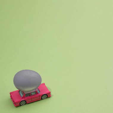Paskalya yumurtası açık yeşil bir yüzey üzerinde eski pembe bir araba tarafından taşınır. Minimalist sahne.
