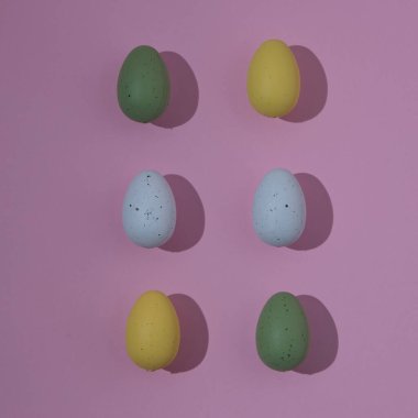 Farklı renklerde Paskalya yumurtaları. Pembe arka planda hafif gölgeler ve sağ tarafta kopyalama alanı var. Minimalist natürmort.