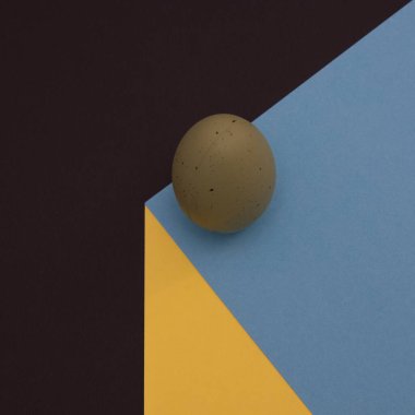 Keskin gölgesi olan koyu yeşil bir Paskalya yumurtası, siyah arkaplanda mavi-sarı bir küpün kenarında duruyor. Asgari Paskalya sahnesi.