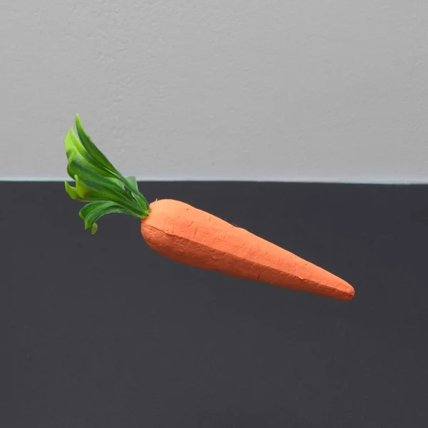 A floating carrot on a black and gray background with copy space. Minimal food scene.