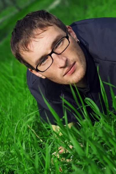 Jonge man in glazen is liyng in groene gras — Stockfoto