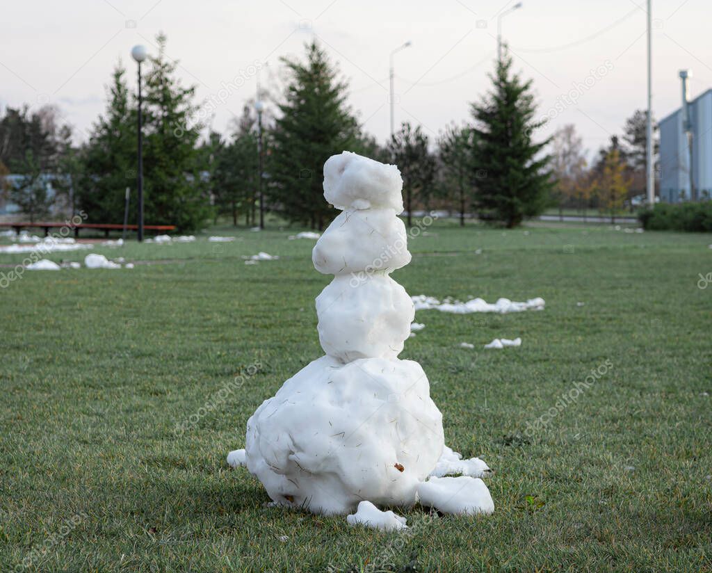 the snowman on the green grass in city