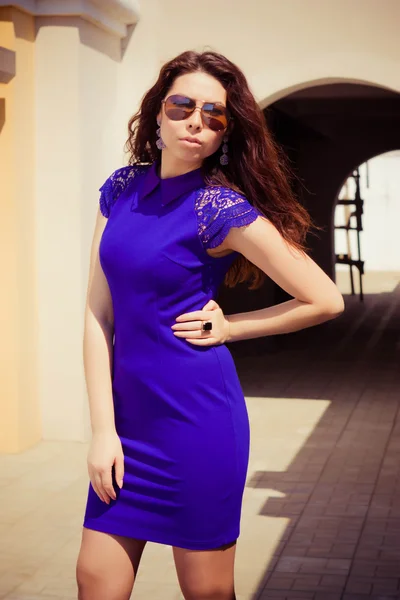 Beautiful sexy woman in a blue dress and sunglasses on the street on a summer day — Stock Photo, Image