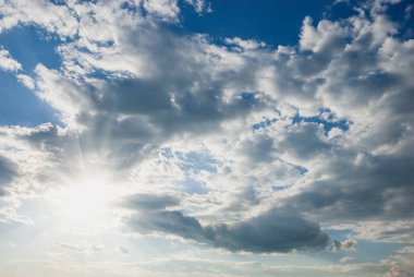Hava beyaz bulutlar, güneş, uzun ışınlar ve mavi gökyüzünde parlıyor. Gökyüzü manzarası