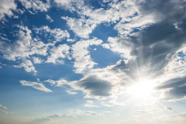Hava beyaz bulutlar, güneş, uzun ışınlar ve mavi gökyüzünde parlıyor. Gökyüzü manzarası