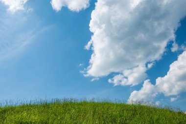 Yeşil çimenli bir tepe ve bulutlu mavi bir gökyüzü.