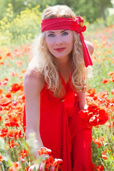 Žena v dlouhé červené šaty mezi makové pole — Stock fotografie