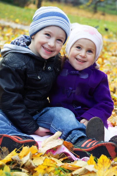 Sister and brother together on autumn leaves — Stock Photo, Image