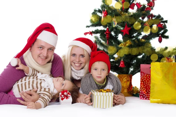 Família feliz com duas crianças em chapéus de Papai Noel sob a árvore de Natal — Fotografia de Stock