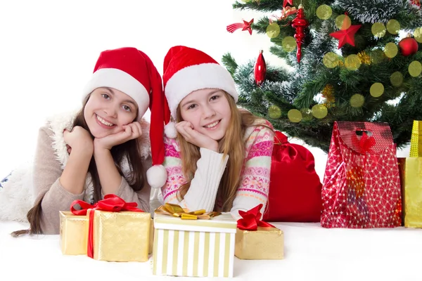 Sœurs souriantes dans les chapeaux de Père Noël couché sous l'arbre de Noël Photo De Stock