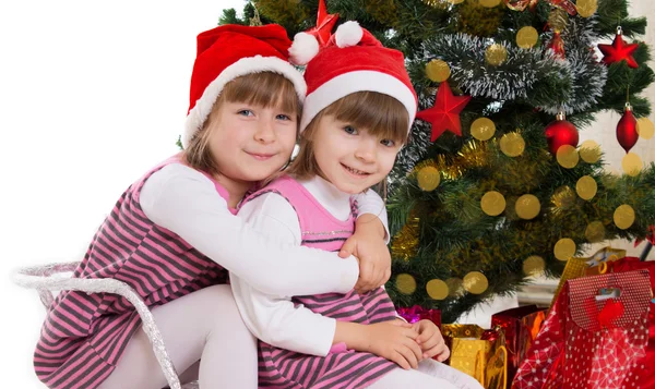 Sisters hugging in sledge under Christmas tree — Stock Photo, Image