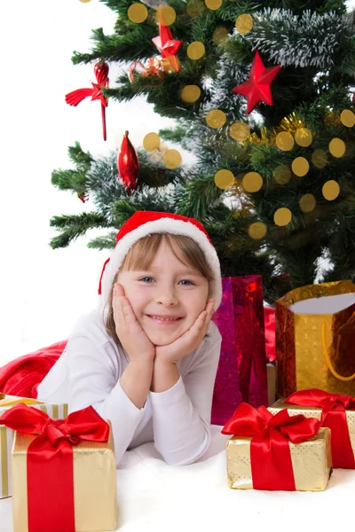 在圣诞老人的帽子，躺在圣诞树下的女孩 图库图片