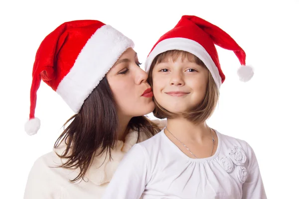Happy mother kissing daughter on cheek in Christmas hat — Stock Photo, Image