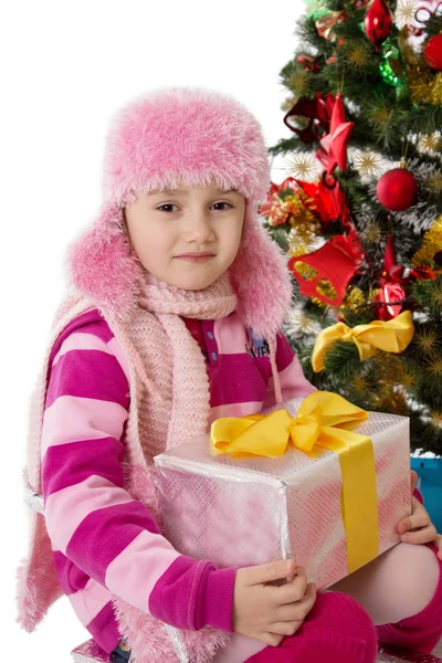 Meisje in roze bont hoed, bedrijf aanwezig onder chritmas boom — Stockfoto