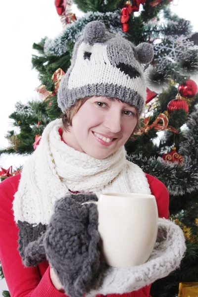 ニットの帽子とミトンをカップとクリスマス ツリーの下の女性 — ストック写真