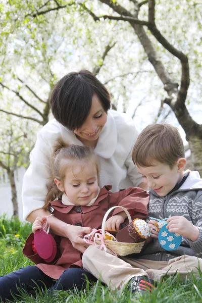 Mutter und zwei Kinder im blühenden Garten mit Osterdekor — Stockfoto