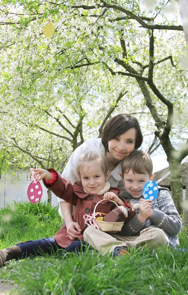 Mutter und zwei Kinder im blühenden Garten mit Ostereiern — Stockfoto