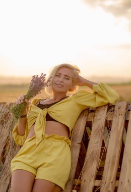 Kırsal alanda sarı giyinmiş, gün batımında altın yulaf tarlası olan genç bir kadın.