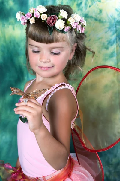 Mooi meisje in een roze jurk met vleugels in een krans op een groen — Stockfoto