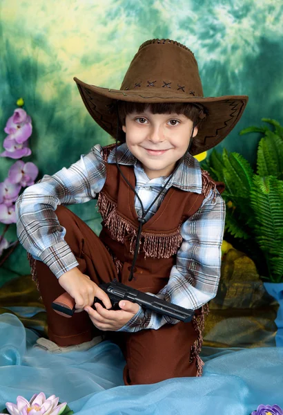 Cute little boy dressed as a cowboy with a gun on a green backgr — Stock Photo, Image