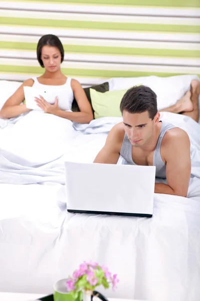Men working on laptop and woman reading book in bedroom — Stock Photo, Image
