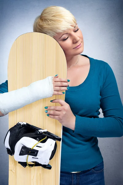 Frau mit gebrochenem Arm umarmt ihr Snowboard — Stockfoto