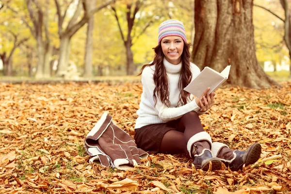 Frau sitzt auf den Herbstblättern und liest Buch — Stockfoto